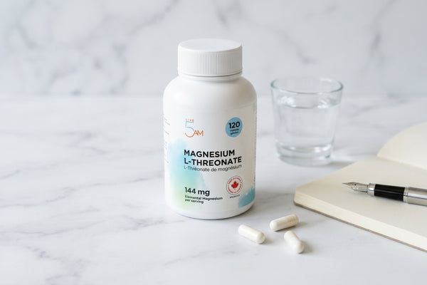 Magnesium L-Threonate bottle on white marble with glass of water, notepad, and white capsules in soft daylight