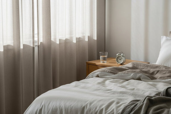 Soft morning light over a neatly made bed with a glass of water on the nightstand, illustrating tiredness after eight hours of sleep.