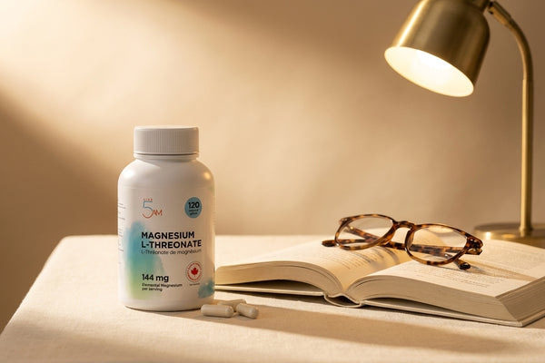 Live 5AM Magnesium L-Threonate bottle on a desk with an open hardcover book, reading glasses, and a small brass desk lamp