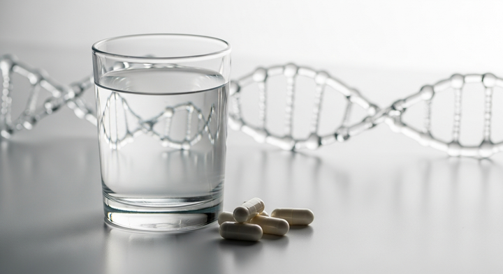 A glass of water and capsules beside a DNA helix model
